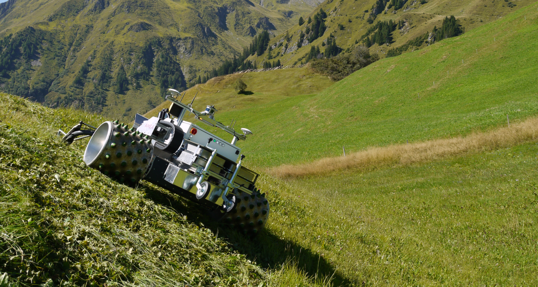 Autonome, vollelektrische Landwirtschaftsmaschine - AMEA Elektrisch betriebener Einachser «AMEA» auf einer grünen Hangwiese vor alpiner Bergkulisse bei sonnigem Wetter.