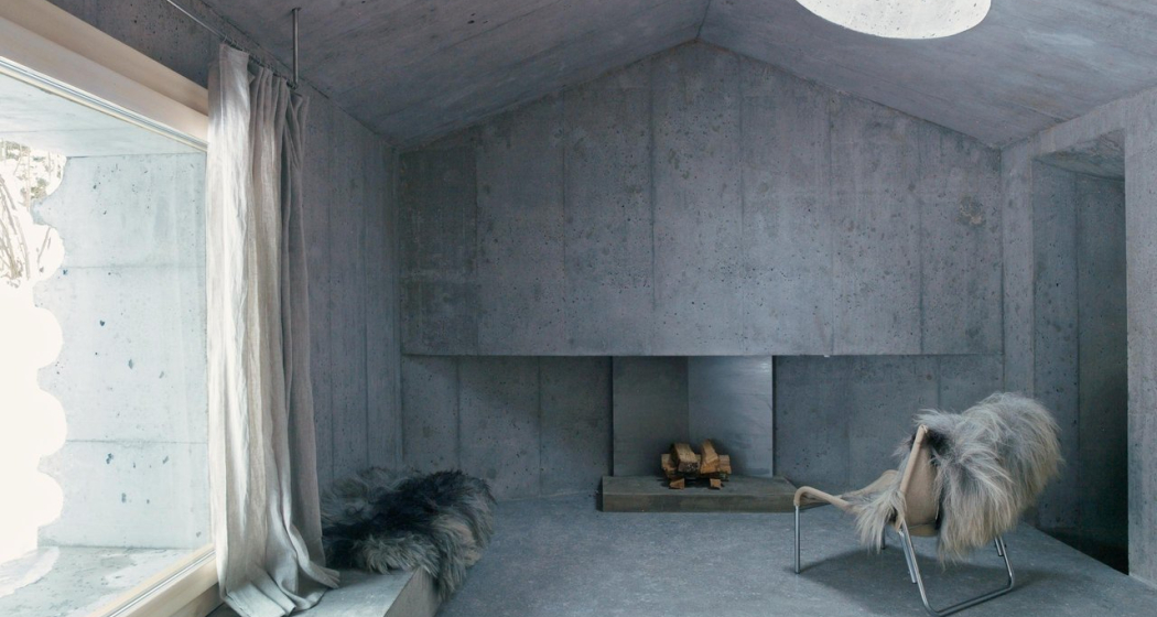 Minimalistischer Raum aus Beton mit Kamin, Sessel und Fell, Lichtöffnung in der Decke
