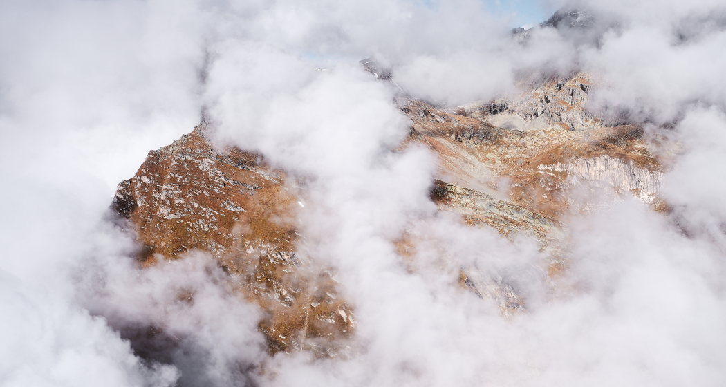 Felsige Berggipfel der Giandas, halb in Wolken gehüllt. Die rotbraunen Felswände ragen dramatisch aus dem Wolkenmeer empor, darüber blauer Himmel. Foto: Gaudenz Danuser.