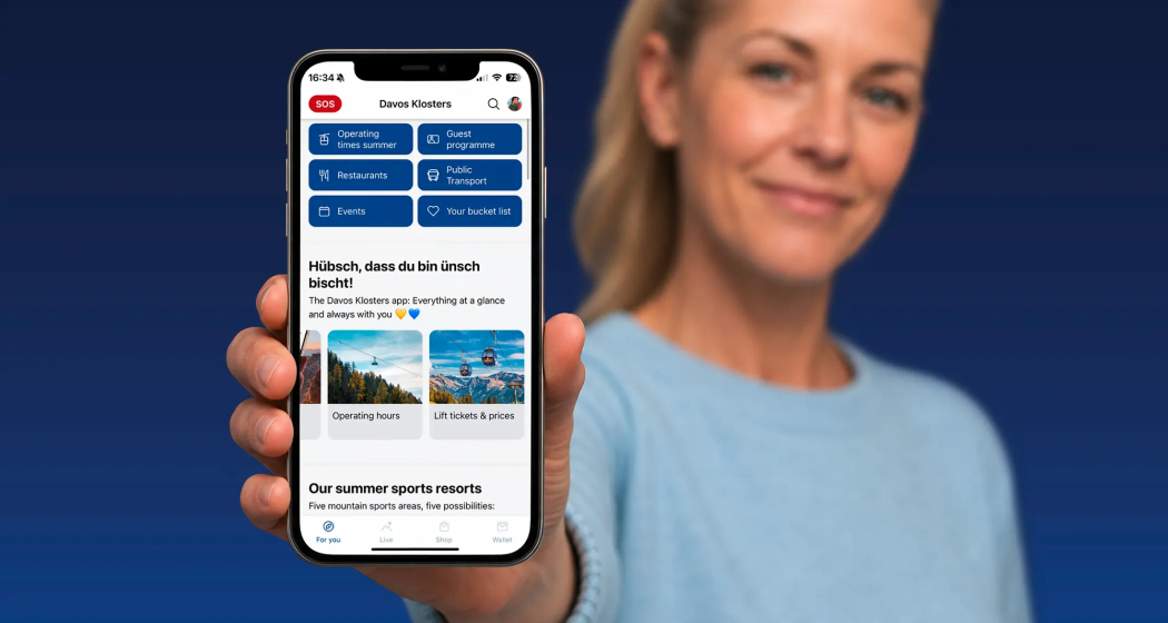Frau hält Smartphone mit geöffneter Davos Klosters App, die Menüpunkte wie Öffnungszeiten, Gästeprogramm, Restaurants, ÖV, Events und Bucket List anzeigt.