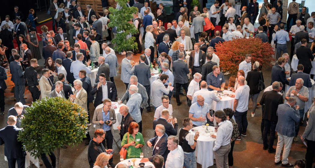 Gäste in Business-Kleidung beim Networking-Apéro an Stehtischen in der Eventhalle des Wirtschaftsforums Südostschweiz.