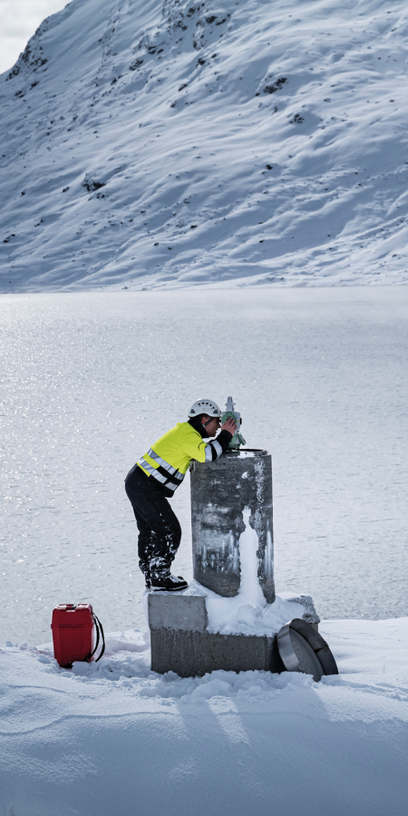 Ein Mann bei Vermessungsarbeiten an einem zugefrorenen Stausee in winterlicher Landschaft in Graubünden