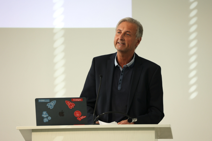 James Cristallo spricht an der Generalversammlung von graubünden digital 2026 am Rednerpult. Vor ihm steht ein Laptop mit GRdigital-Stickern. Im Hintergrund ist eine Projektionsfläche zu sehen.