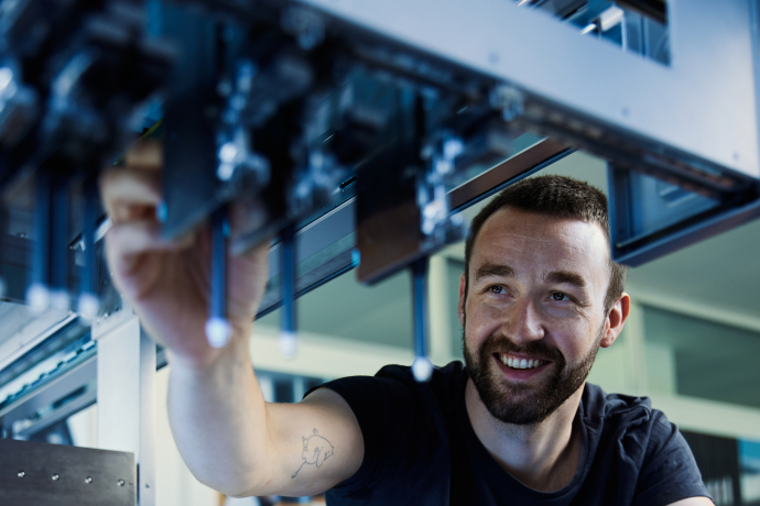 Lächelnder Mitarbeiter arbeitet an einer Produktionsmaschine in einer Fabrikhalle.