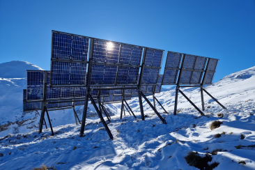 Solaranlage in alpiner Schneelandschaft mit blauen Photovoltaikmodulen vor klarem Himmel.
