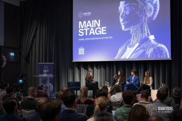 Publikum bei einer Podiumsdiskussion des Swiss AI Summit mit vier Personen auf der Bühne vor einer Leinwand mit der Aufschrift Main Stage, Panel Discussions & Keynotes