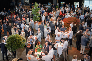 Gäste in Business-Kleidung beim Networking-Apéro an Stehtischen in der Eventhalle des Wirtschaftsforums Südostschweiz.